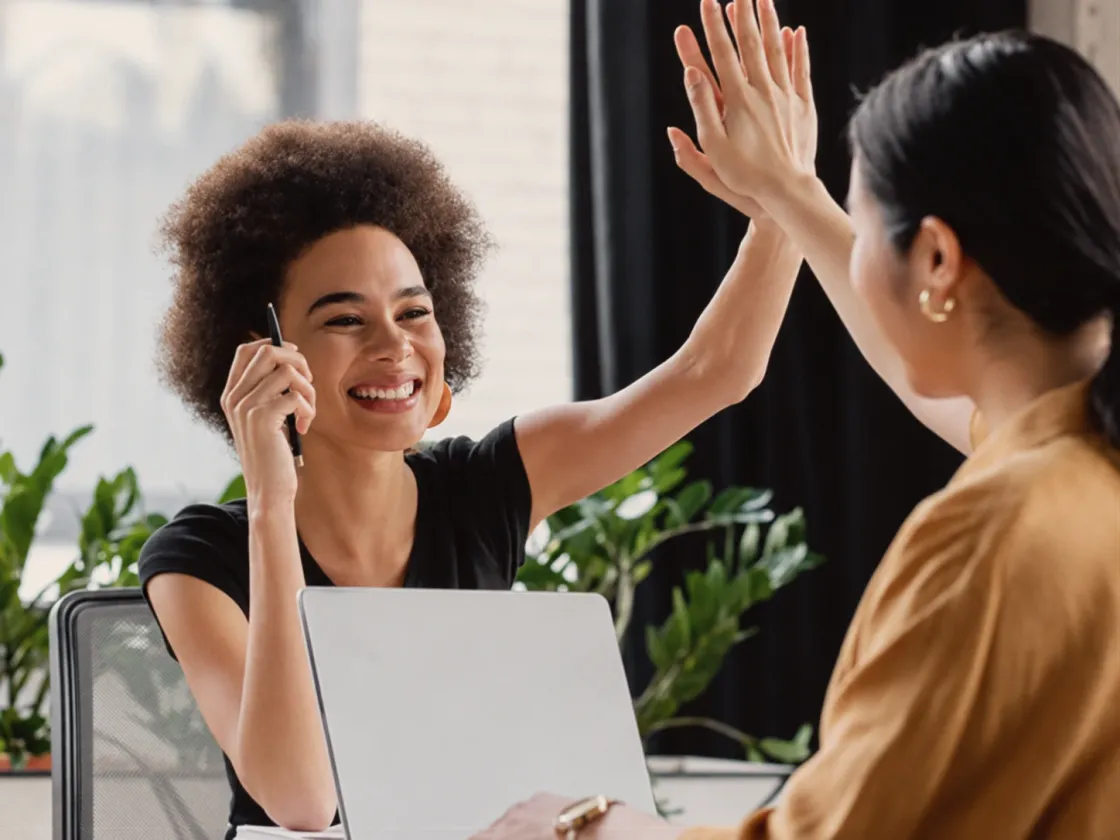A coach and a client high-fiving across a desk