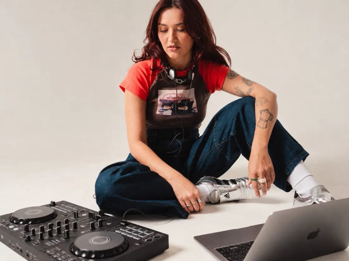 Someone sitting on the floor with a DJ controller and a laptop