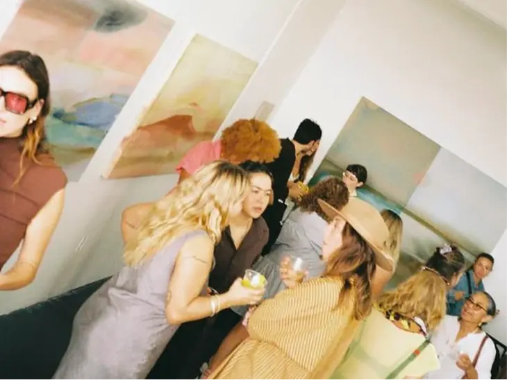 Guests chatting at a gallery opening, paintings on the walls