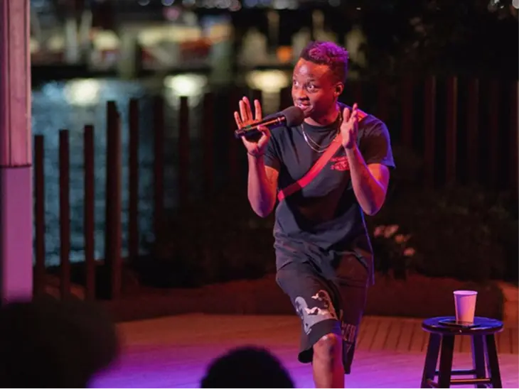 A comedian performing on a small stage under purple lights