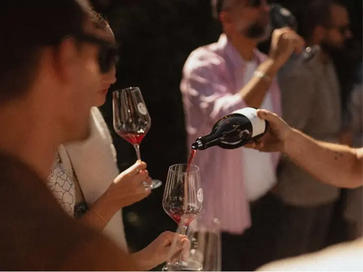 A host pouring red wine for guests at a tasting