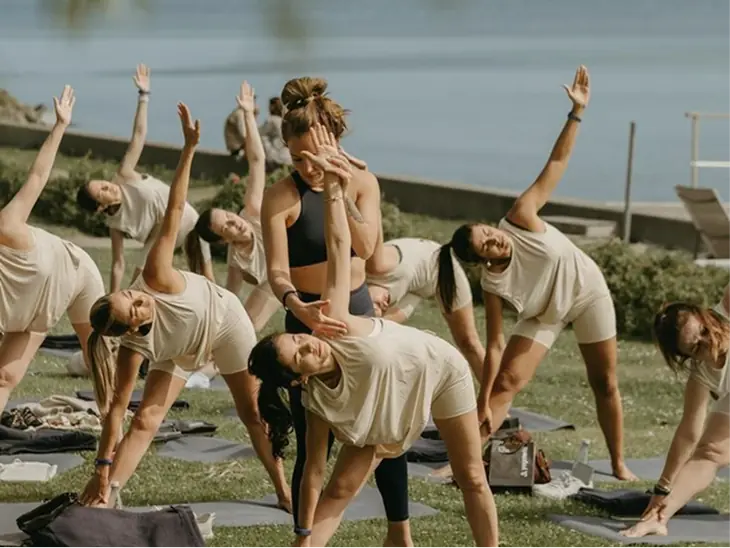 A group doing a yoga stretch together outdoors by the sea