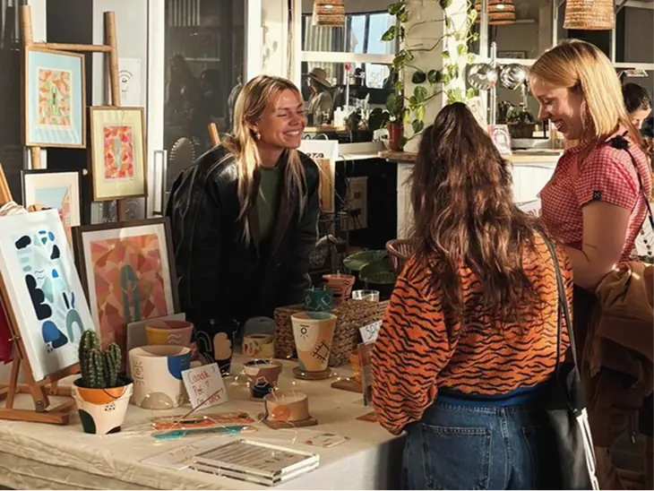 Shoppers browsing handmade prints and pottery at a pop-up market